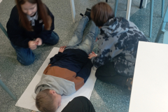 Bērns guļ uz uzemes uz paklāja, kāmēr divi bērni taisa kaut kādu eksperimentu