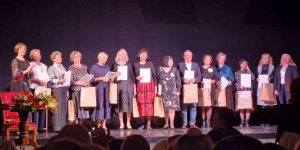 Skolotāji stāv uz skatuves ar diplomiem