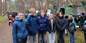 9.a klases skolnieki Ādažu militārajā poligonā kopbilde priekšā militārajai mašīnai.