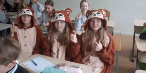 Bērni saģērbti susļiku tērpos sēz pie soliem