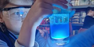 Bērns spīdina ar lukturīti glāzi kurā ir zils šķidrums