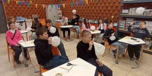 Skolēni sēž kabinetā pie galdiem un klausās prezentāciju