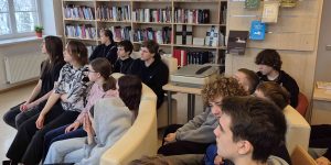 Bērni sēž bibliotēkā un klausās prezentāciju