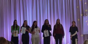 Skolēni stāv uz skatuves ar pateicības rakstu