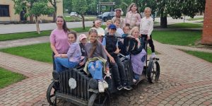 2.b klase sasēdusies uz veca auto statujas bildei